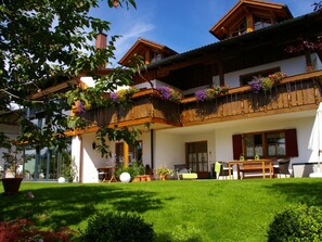A two-story wooden house with a balcony, a dining area with outdoor furniture, and a well-maintained lawn. - Aggenstein House Mountain View (Rieden am Forggensee)
