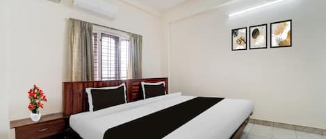 A hotel room with a bed, bedside table, and a window with curtains.