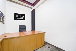 A hotel reception desk with a sign above it, a chair, and a wall-mounted key rack.