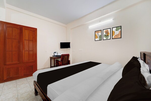 A bedroom with a bed, a wooden wardrobe, a desk with a chair, and three framed artworks on the wall.
