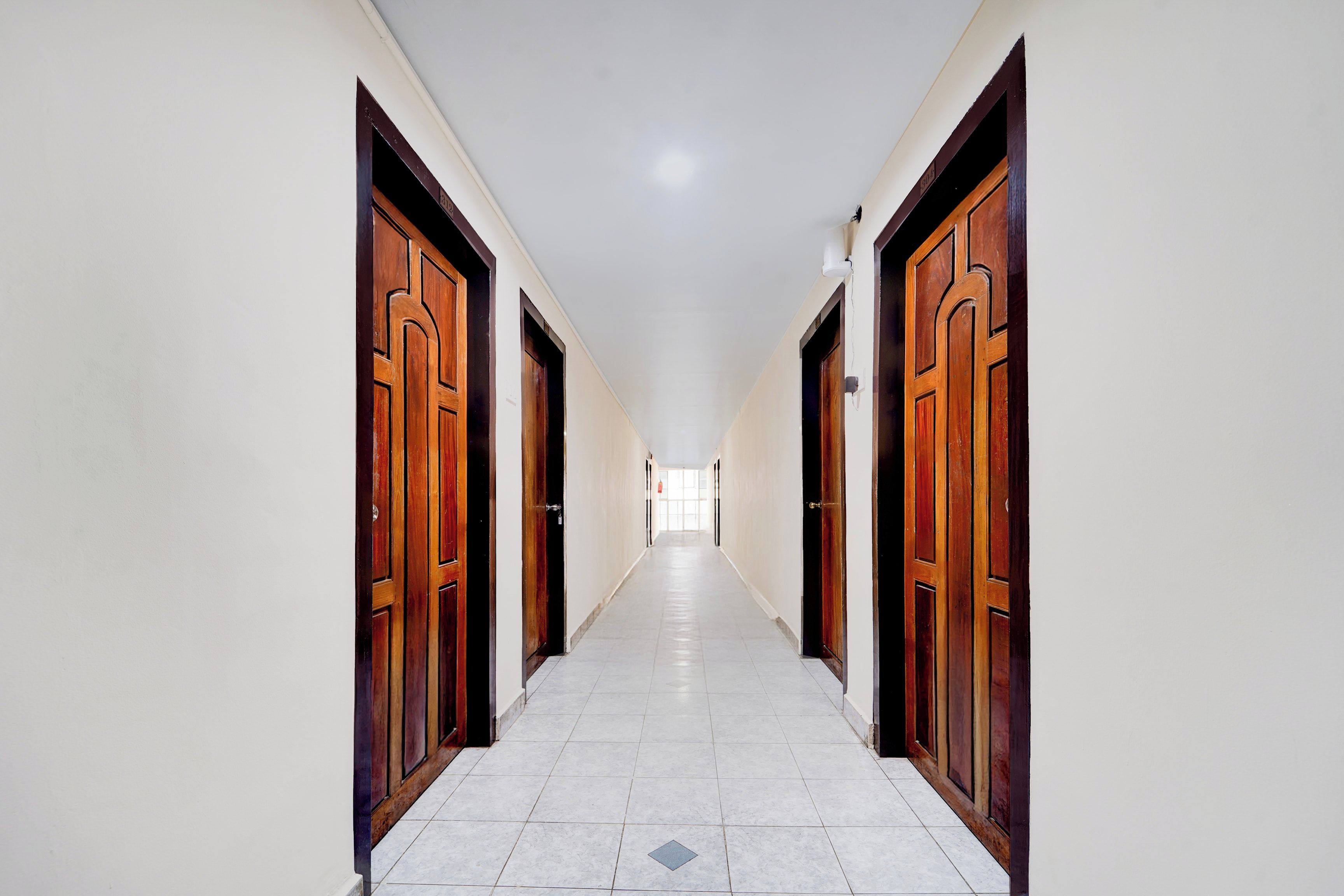 A corridor with doors on both sides, leading to a bright room at the end.