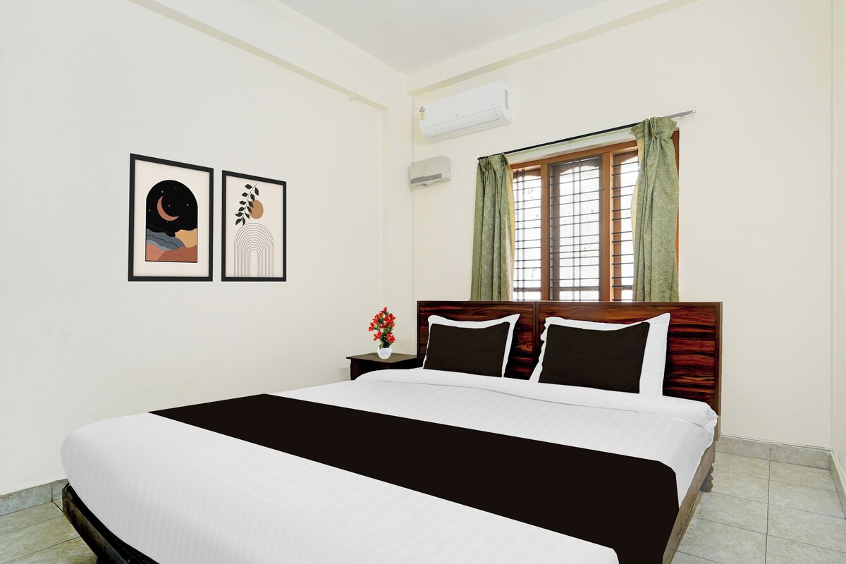 A hotel room with a bed, a nightstand with a vase of flowers, and two framed pictures on the wall.