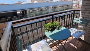 Ein Balkon mit Tisch und Stühlen, einem Blumentopf und Blick auf Gebäude im Hintergrund.