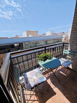 Un balcone con tavolo e sedie, una pianta in vaso e vista su edifici sullo sfondo.