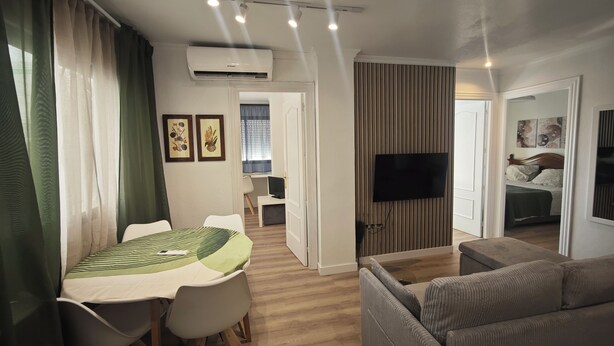 Ein modernes Wohnzimmer mit einer Couch, einem Esstisch mit Stühlen, einem flachbildfernseher an der Wand und einer Klimaanlage.