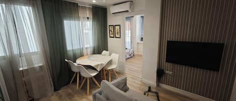 Una sala moderna con comedor, un sofá, un televisor montado en la pared y un equipo de aire acondicionado.