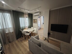 Una sala moderna con comedor, un sofá, un televisor montado en la pared y un equipo de aire acondicionado.