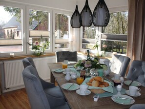 A breakfast table set with plates, cups, and a basket of pastries, with a view of trees and a building outside. - Holiday Home With 4 Bedrooms (Osterhever)