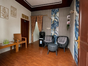 A room with a wooden floor, two upholstered chairs, a bench, a water dispenser, and a door with a decorative panel.