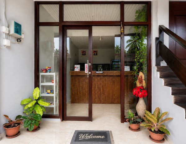 A reception area with a wooden reception desk, a 'Welcome' mat, and potted plants. - Hotel O near Pantai Manggar (Samboja Kuala)