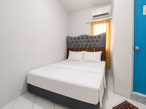 A hotel room with a bed, an air conditioning unit, a blue door, and a window with curtains.