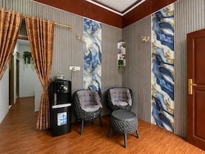 A room with a water dispenser, two cushioned chairs, a small stool, and a door with a decorative panel. - Hotel O near Pantai Manggar (Samboja Kuala)