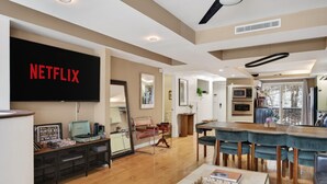 A modern living room with a large flat-screen TV, wooden flooring, a dining area with a wooden table and chairs, and a kitchen with built-in appliances. - 2-Level Cabin @ Scribners | Huge Spa & 3 Balconies (Tannersville)