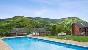 A swimming pool with a view of green hills and a fenced area with buildings. - 2-Level Cabin @ Scribners | Huge Spa & 3 Balconies (Tannersville)