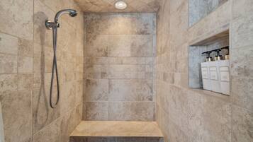 A shower with a handheld showerhead, a built-in shelf with toiletries, and a recessed ceiling light.