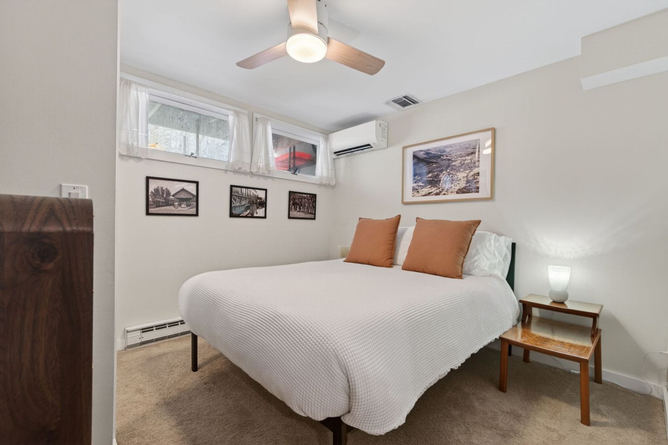 Une chambre à coucher avec un lit, une table de chevet avec une lampe, un ventilateur de plafond, une fenêtre avec des rideaux et des tableaux encadrés accrochés au mur.