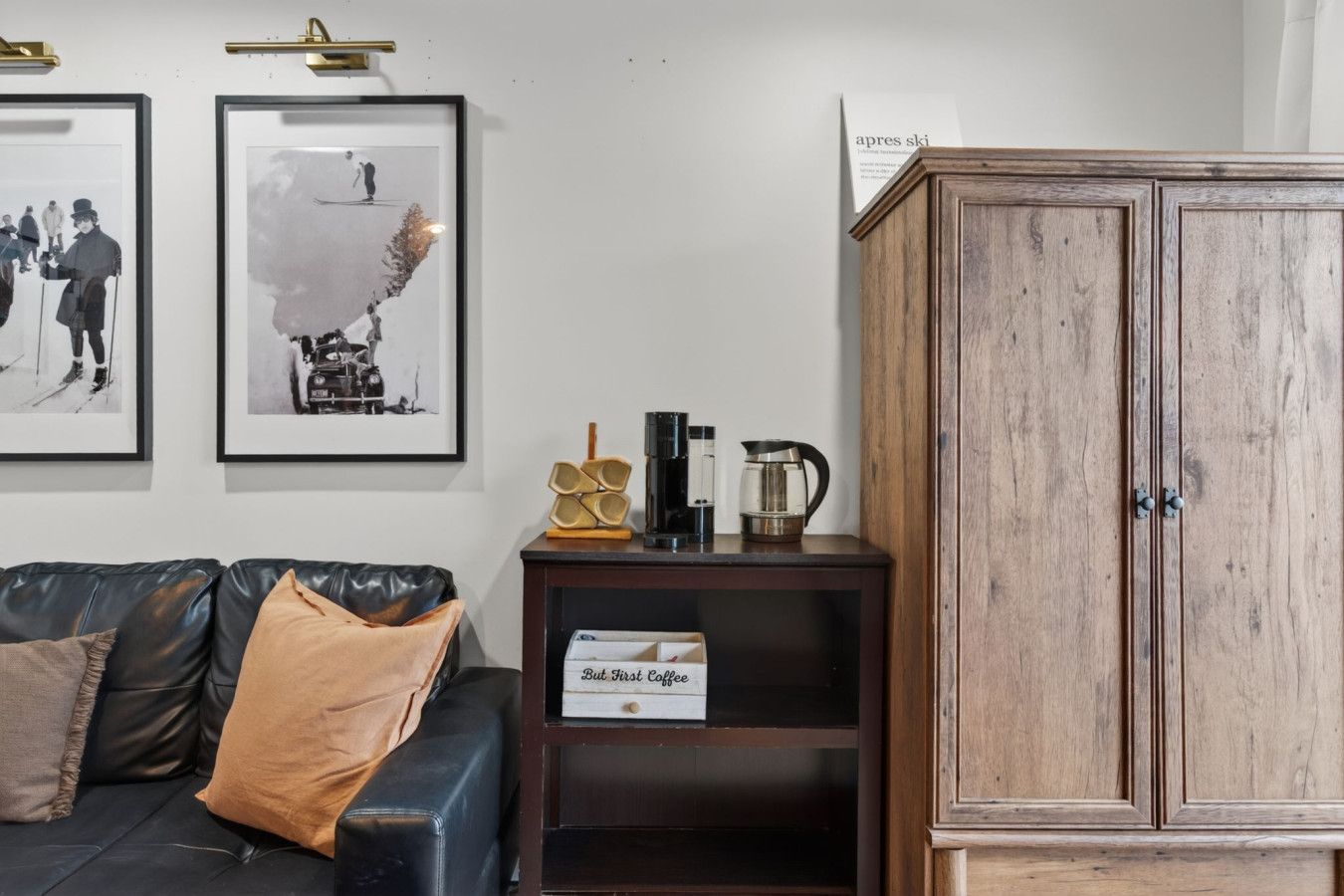 Una sala de estar con un sofá de cuero, un mueble de madera y dos fotografías enmarcadas en la pared.
