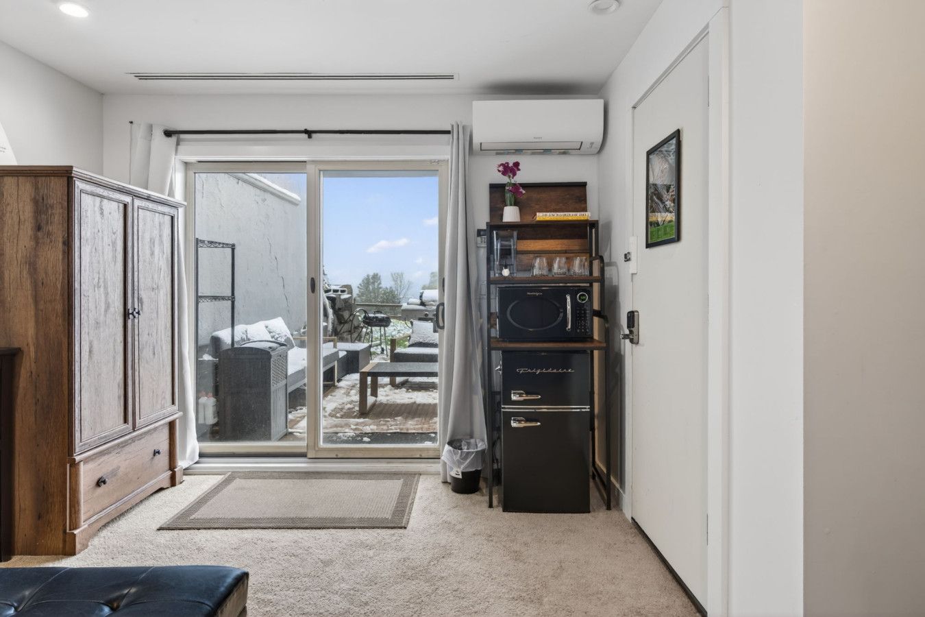 Un espace de vie compact doté d’une porte-fenêtre coulissante donnant sur une zone extérieure, d’un four à micro-ondes encastré et d’un petit coin salon.