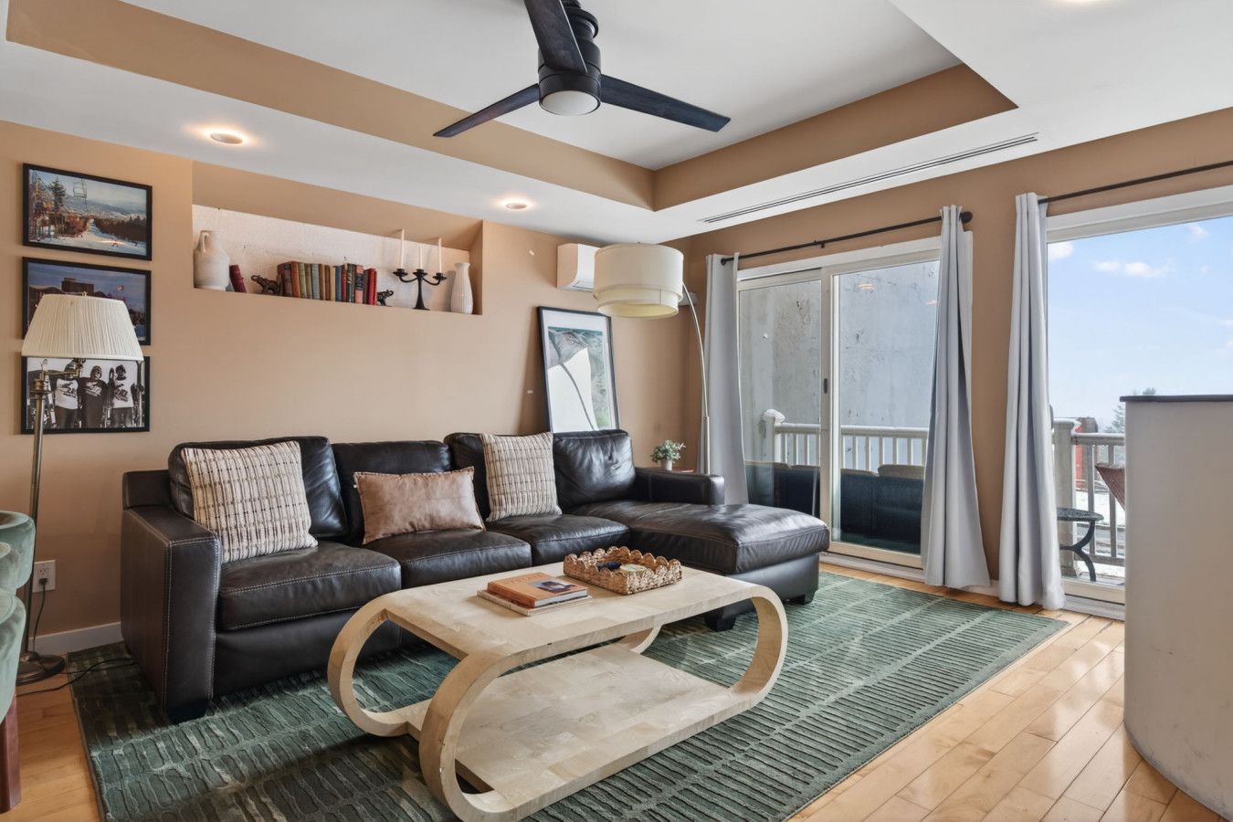 Un salon moderne avec un canapé en cuir, une table basse en bois et une grande porte-fenêtre coulissante donnant sur un balcon.