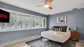 A bedroom with a bed, nightstands, a ceiling fan, a window with blinds, and a wall-mounted TV.