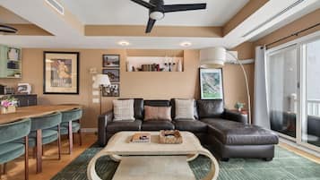 A modern living room with a sectional sofa, a dining table, and a ceiling fan.