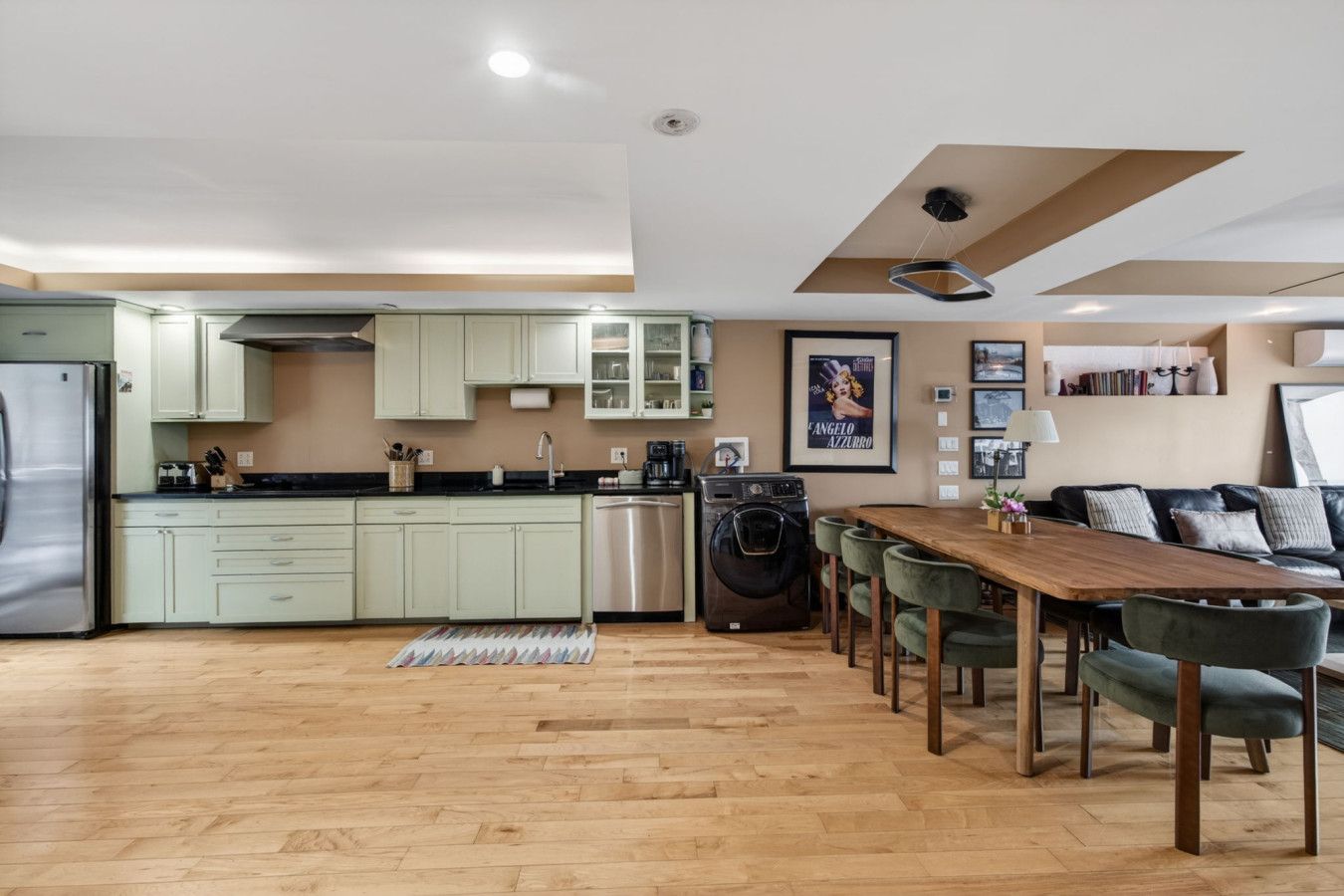 A modern kitchen with light green cabinets, a wooden dining table, and a washing machine.