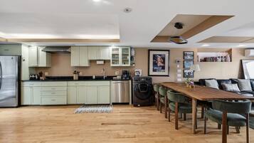 A modern kitchen with light green cabinets, a wooden dining table, and a washing machine.