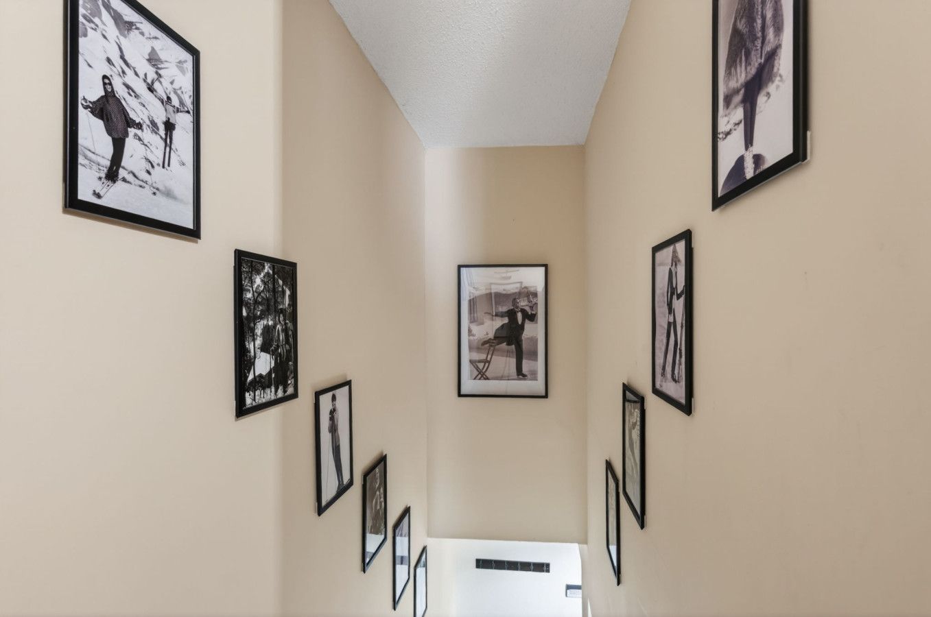 A hallway with framed pictures on the walls, leading to a room with a white door.