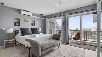 A bedroom with a bed, bedside tables, a chair, a balcony with a chair, and a ceiling fan.