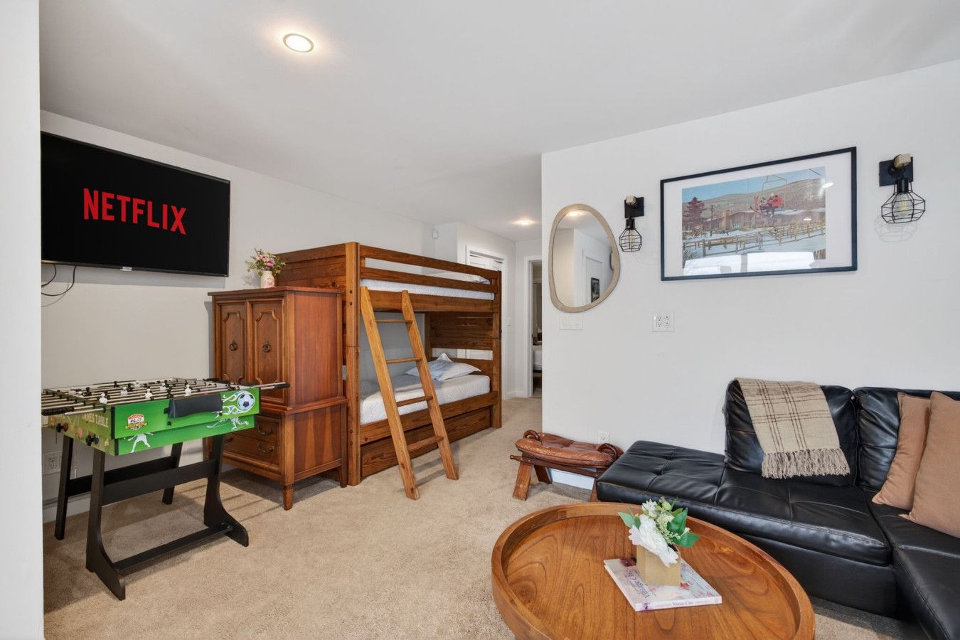 Una habitación amoblada con una cama litera, una mesa de fútbol, un sofá de cuero, una mesa de centro, un televisor y un cuadro en la pared.