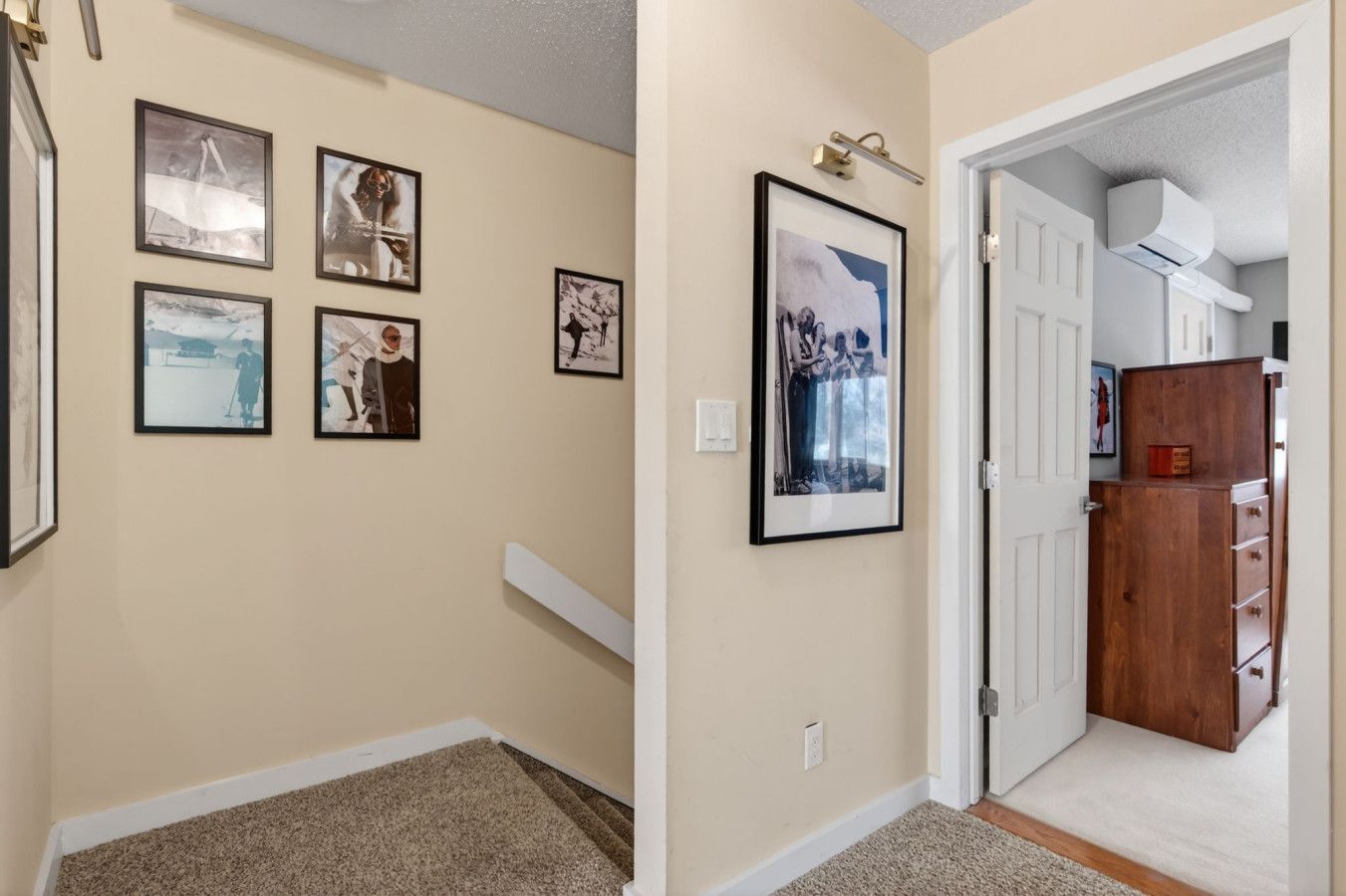 Un couloir avec des tableaux encadrés accrochés au mur, une porte blanche et un meuble en bois doté de tiroirs.