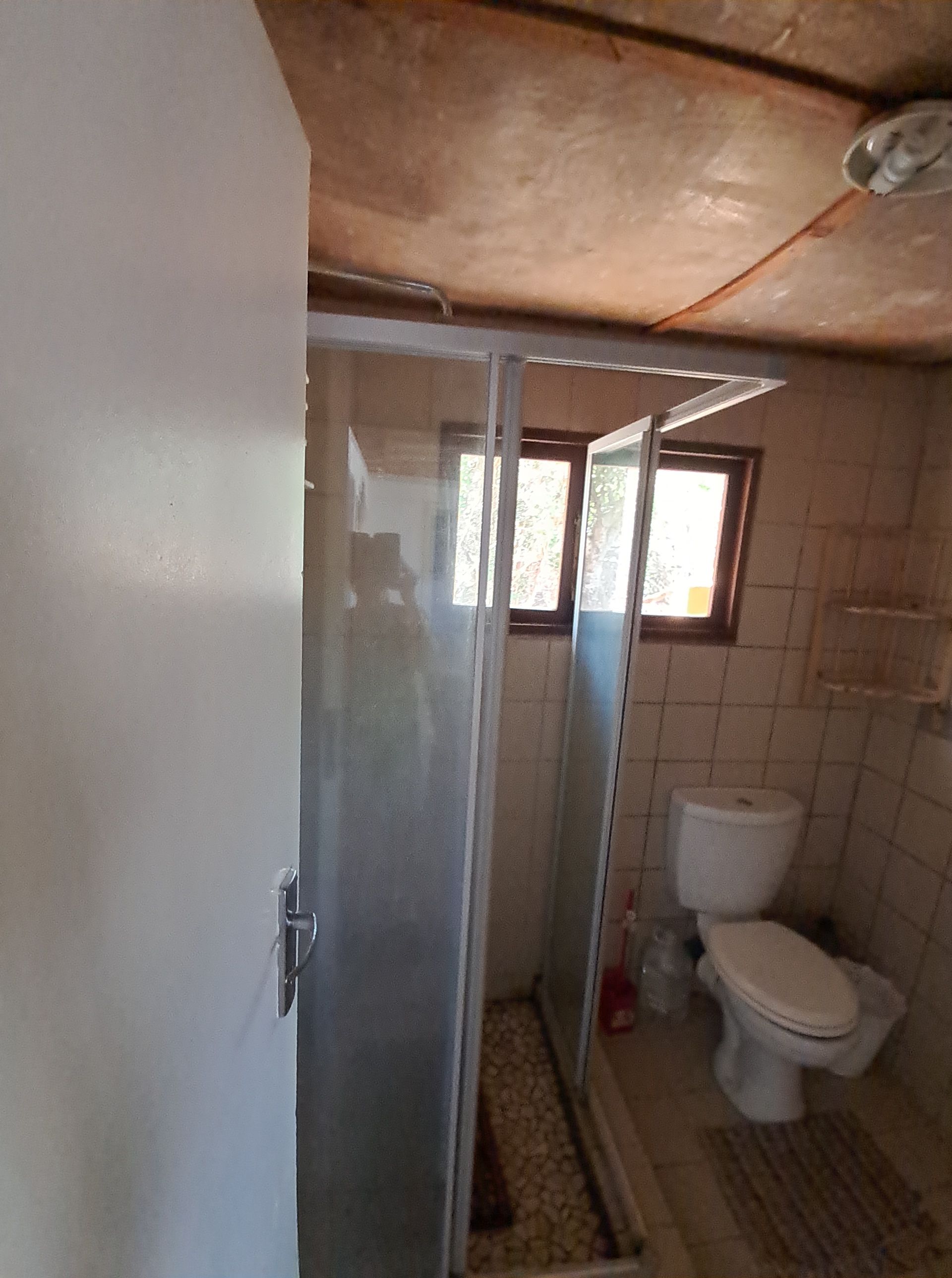A bathroom with a glass shower enclosure, a toilet, and a tiled floor.
