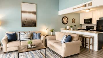 A living room with two sofas, a coffee table, and a kitchen area with a microwave and stove.