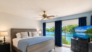 A bedroom with a bed, a nightstand, a dresser, a television, and a view of a lake. - Sunset Shores Lakefront Views Pool and Lakeview (Lake Ozark)