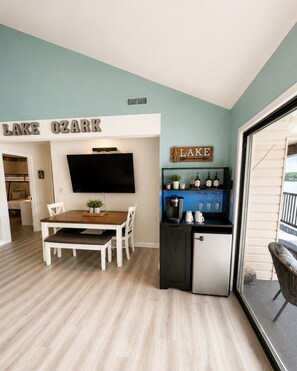 Un espacio habitable compacto con comedor, kitchenette y televisor montado en la pared.
