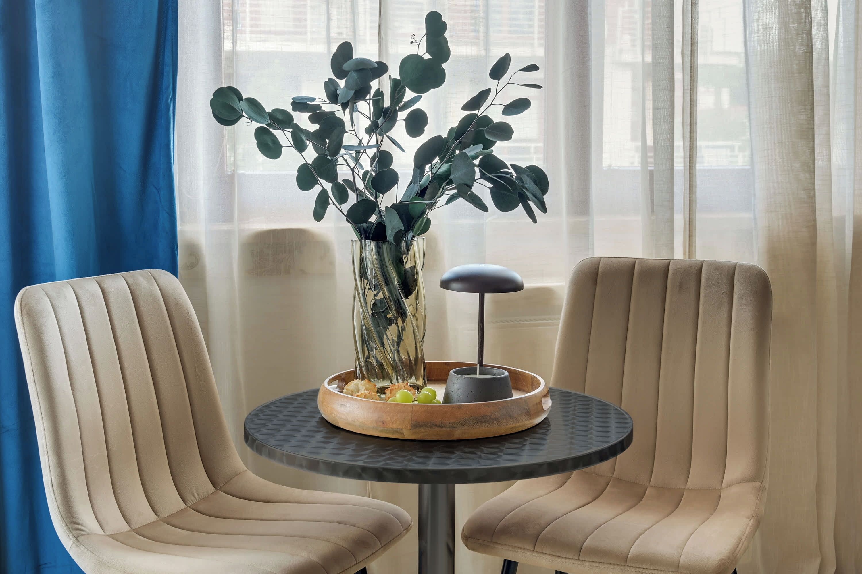 Quarto com duas cadeiras bege, uma mesa redonda pequena com um vaso de folhagem verde e um objeto decorativo.