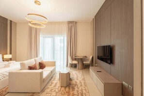 Een moderne hotelkamer met een bank, een klein rond tafeltje, een flatscreen televisie aan de muur en een groot raam met gordijnen.