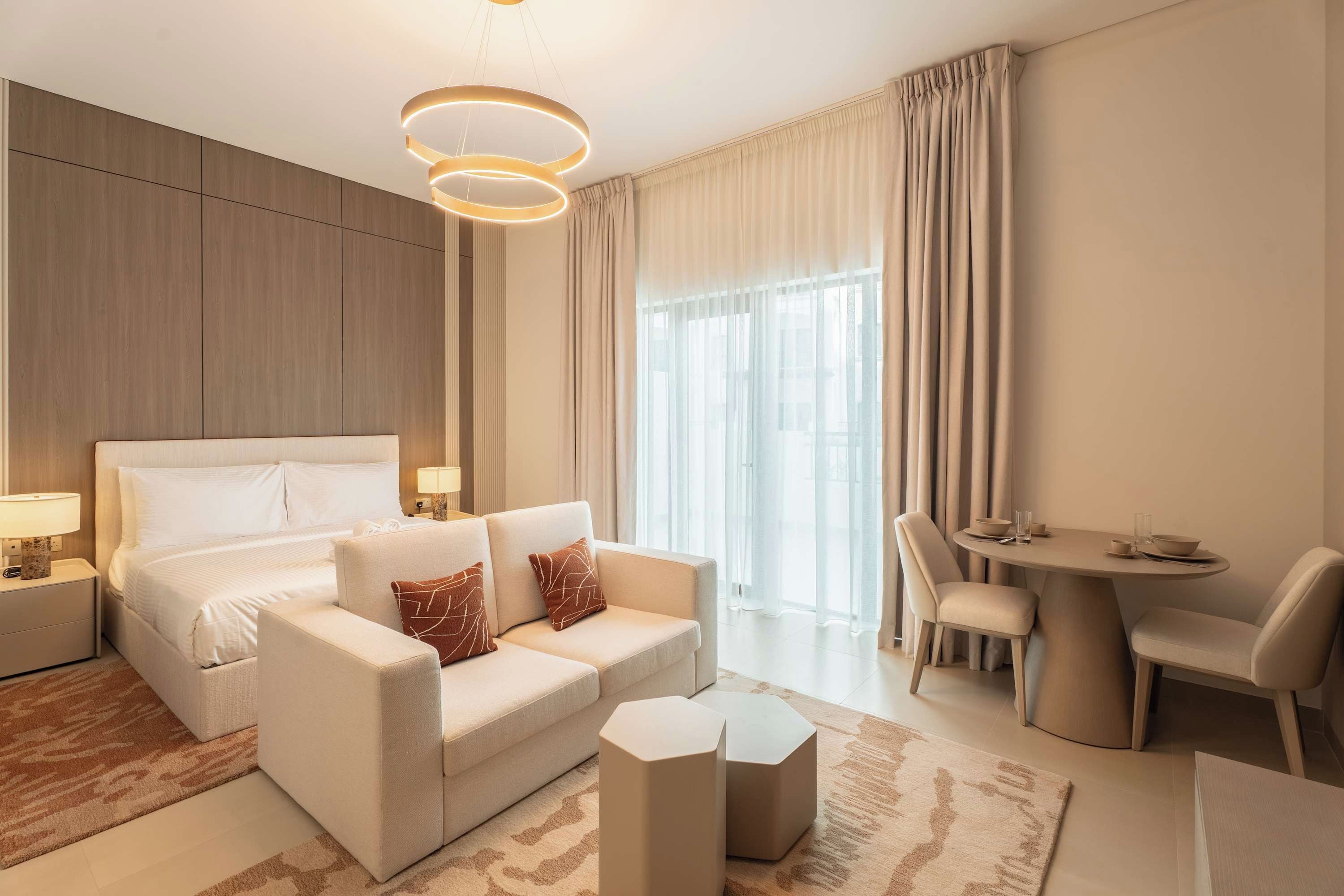 A modern hotel room with a bed, a sofa, a dining table, and a chair.