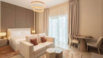A modern hotel room with a bed, a sofa, a dining table, and a chair.