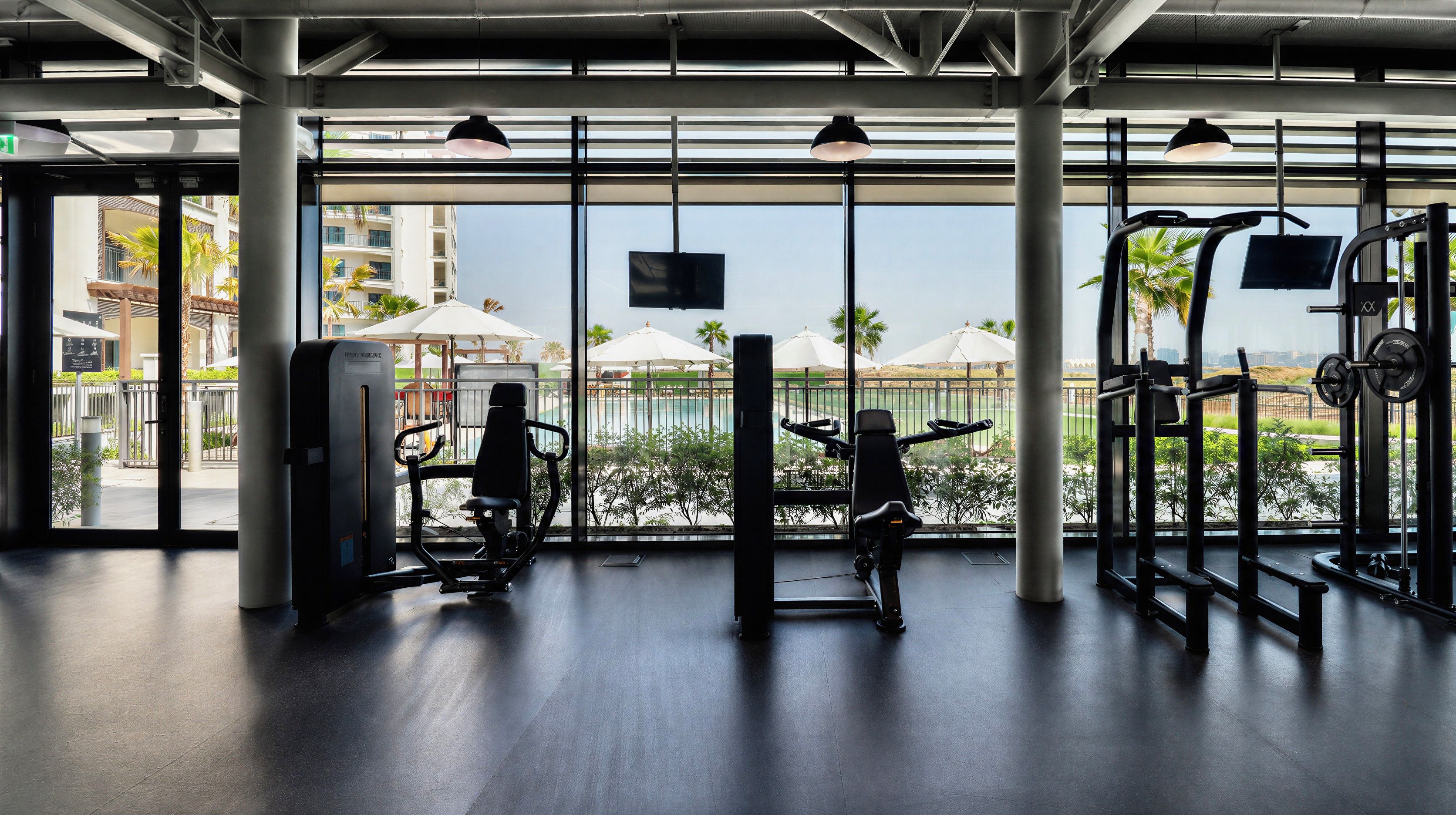 A gym with exercise equipment and a view of a pool and palm trees.