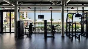 Een sportschool met trainingsapparatuur en uitzicht op een zwembad en palmbomen.