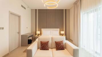 A modern hotel room with a large bed, two bedside tables with lamps, a sofa, and a large window with curtains.