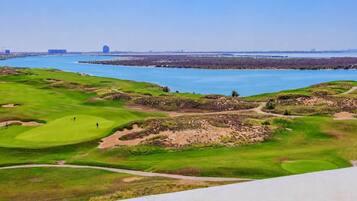 A golf course with bunkers, a water body, and distant buildings.