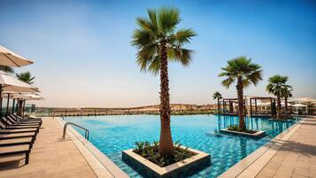 A swimming pool with lounge chairs and umbrellas, surrounded by palm trees.