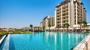 A hotel with a swimming pool, multiple balconies, and palm trees.