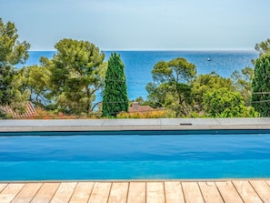A swimming pool with a wooden deck, surrounded by trees and a view of the sea. - Villa in Les Issambres With Swimming Pool (Roquebrune-sur-Argens)
