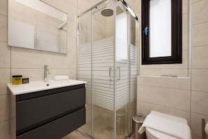 Une salle de bain moderne avec une douche à l’italienne en verre, un meuble-lavabo avec un placard foncé et un grand miroir au-dessus du lavabo.