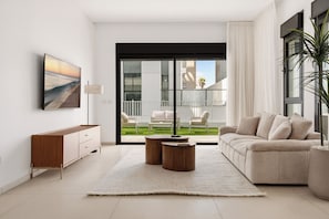 Un salon moderne comprenant un canapé, une table basse, un téléviseur et donnant sur un balcon aménagé avec du mobilier d’extérieur.