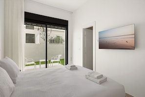Une chambre d’hôtel avec un lit, un balcon avec des chaises et un tableau représentant une scène de plage.