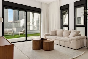 A modern living room with a sofa, two side tables, a view of a balcony, and a large window. - Spacious 4BR Luxury l Balcony & Mamad (Petah Tikva)